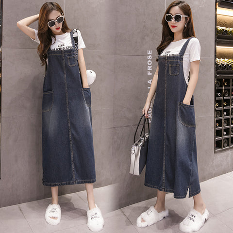 Woman wearing a denim dress with sunglasses and white shoes in front of a gray wall.